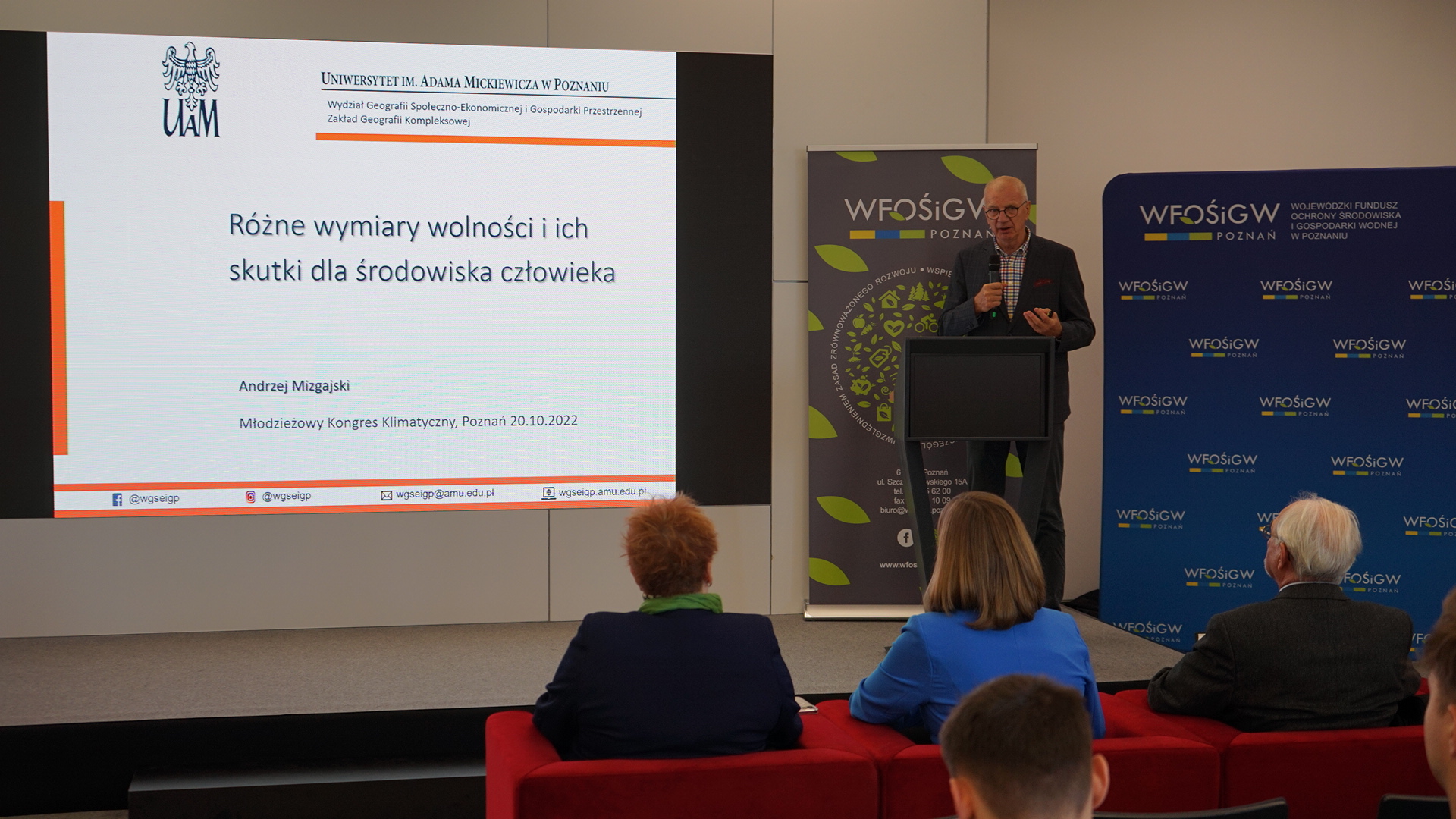 Jedna osoba stoi na scenie przy mównicy.