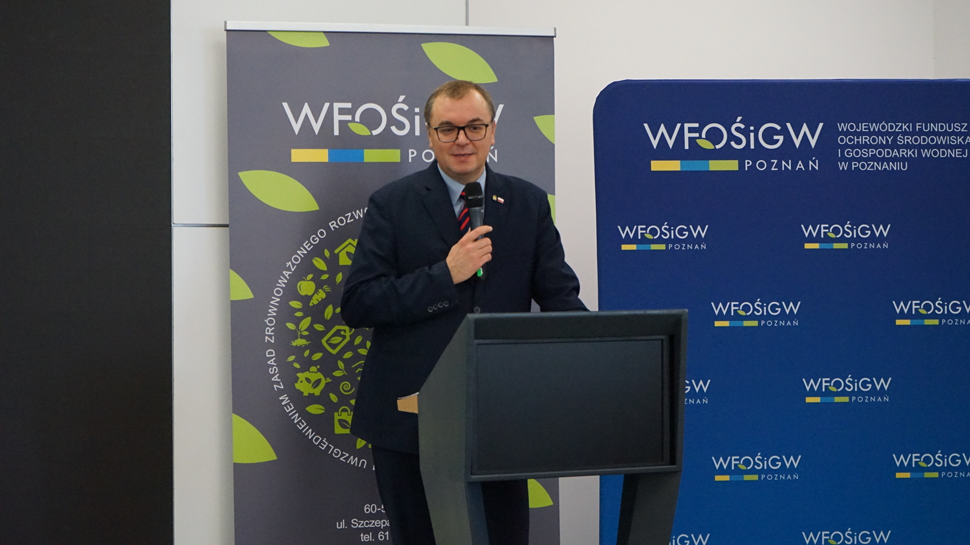 Jedna osoba stoi na scenie przy mównicy.