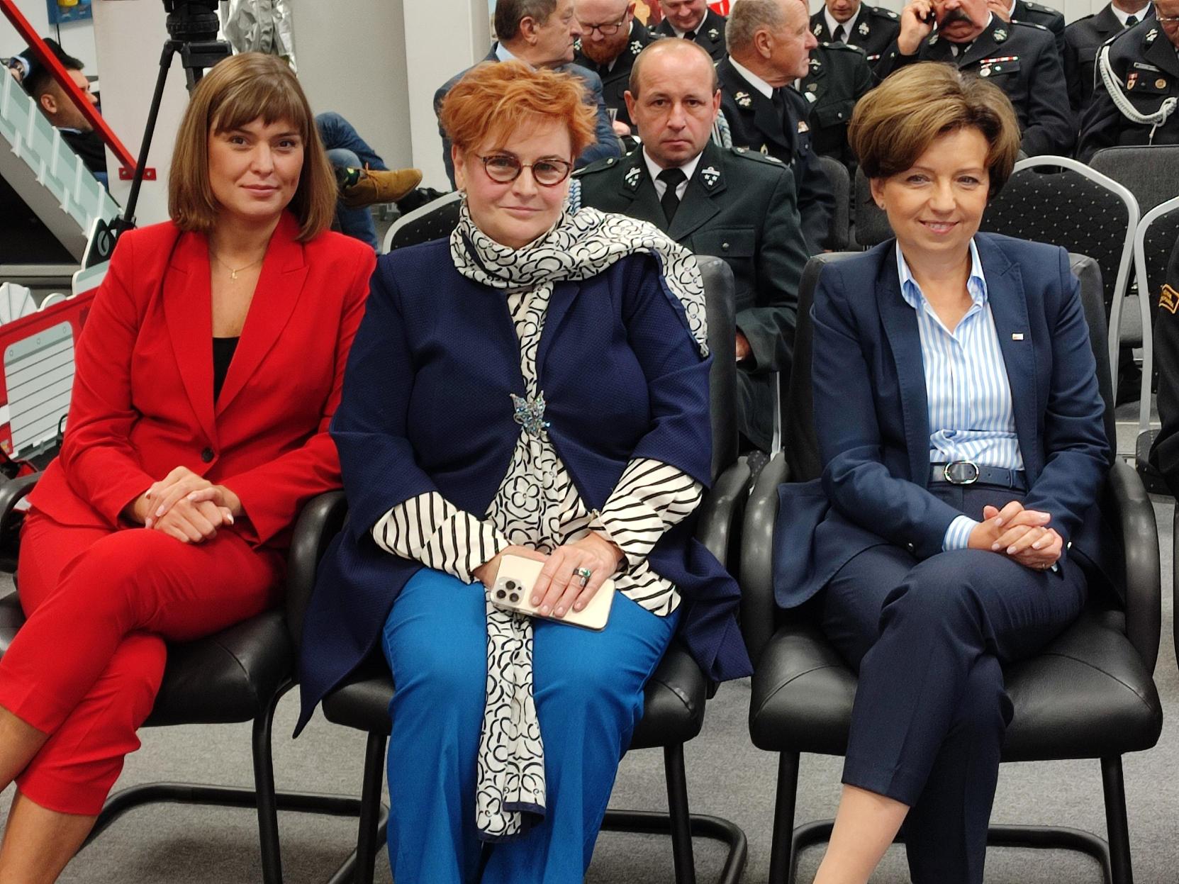 3 osoby siedzą na krzesłach.