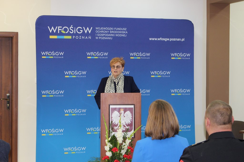 1 osoba stoi na tle ściany przy mównicy.