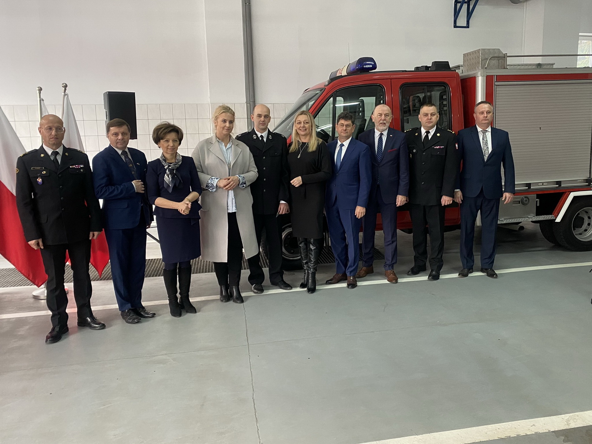 10 osób stoi na tle ściany i samochodu.