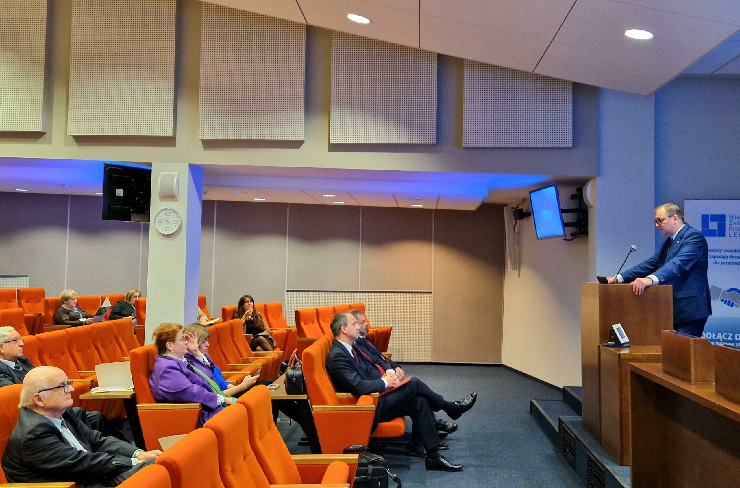 Widok sali i 1 osoba stoi przy mównicy.