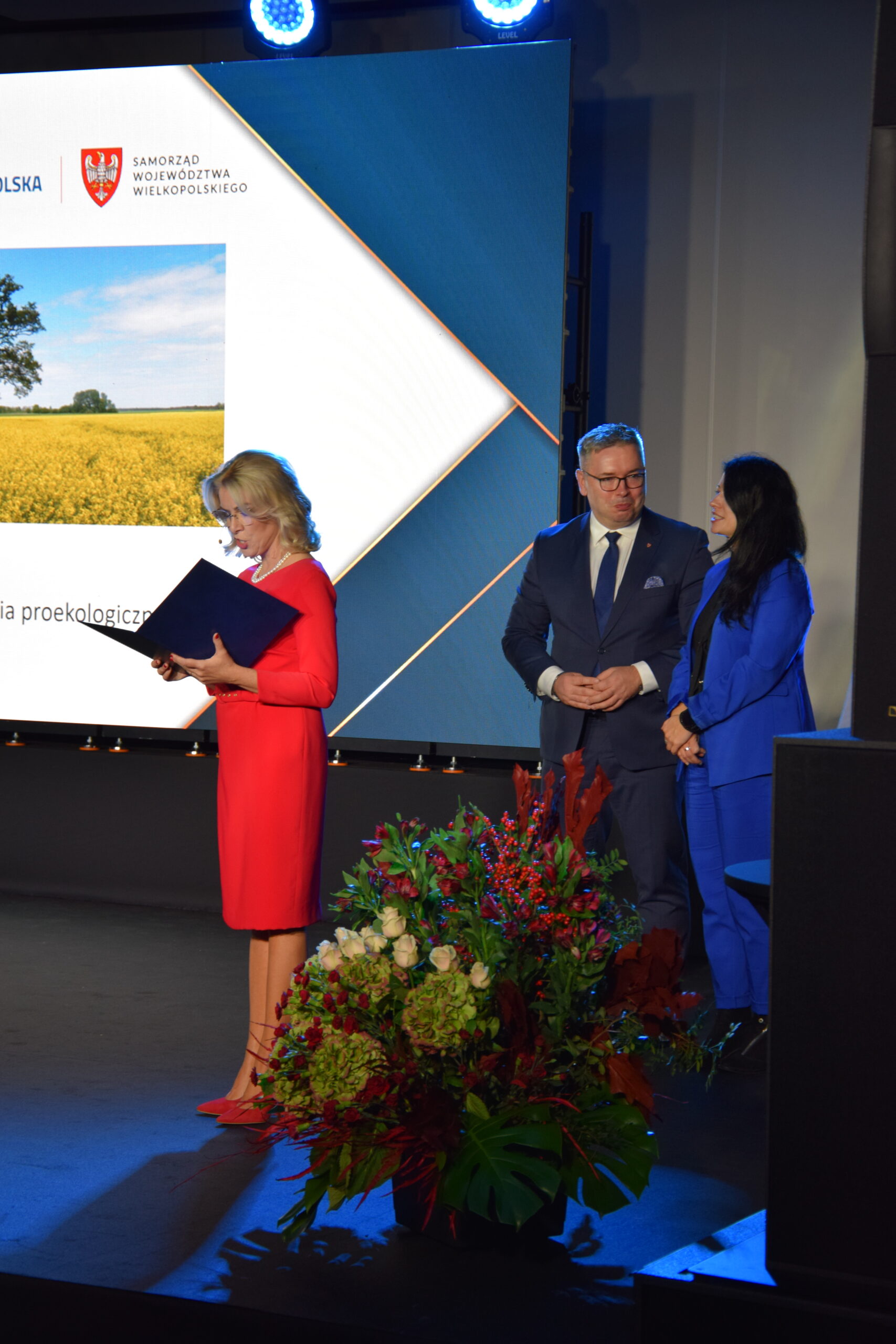 3 osoby stoją na scenie.