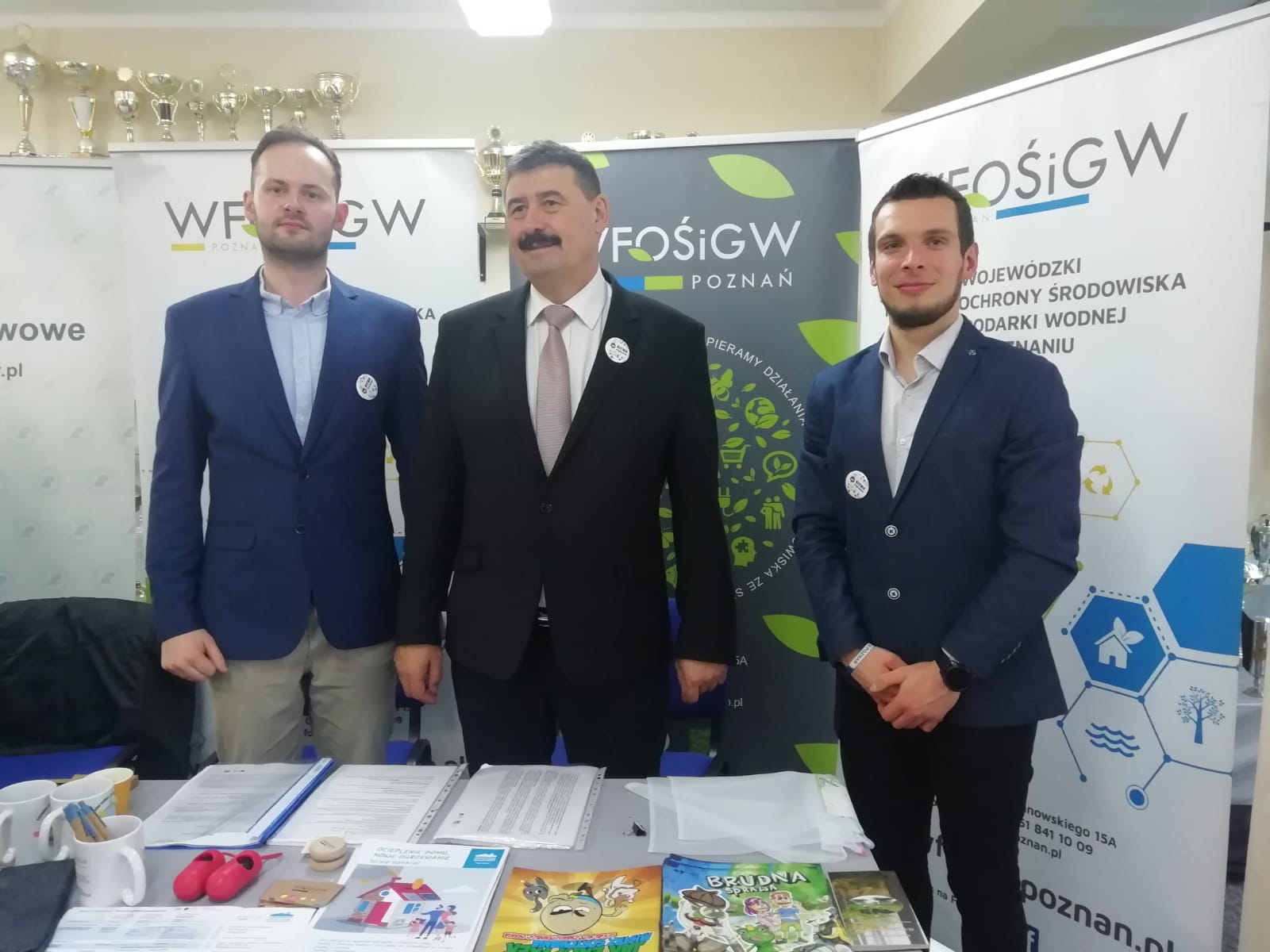 3 osoby stoją na tle ściany.