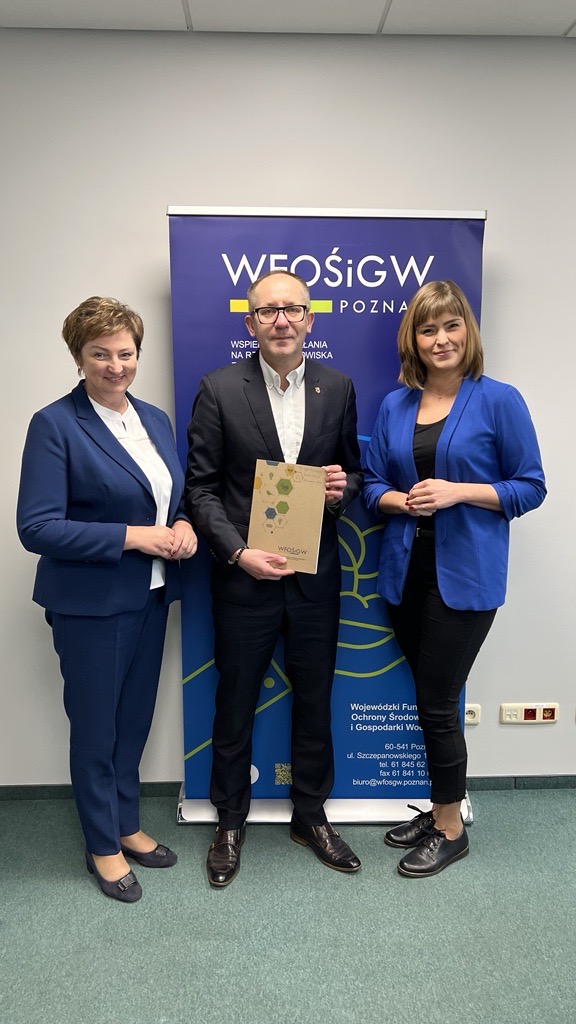 3 osoby stoją na tle ściany.