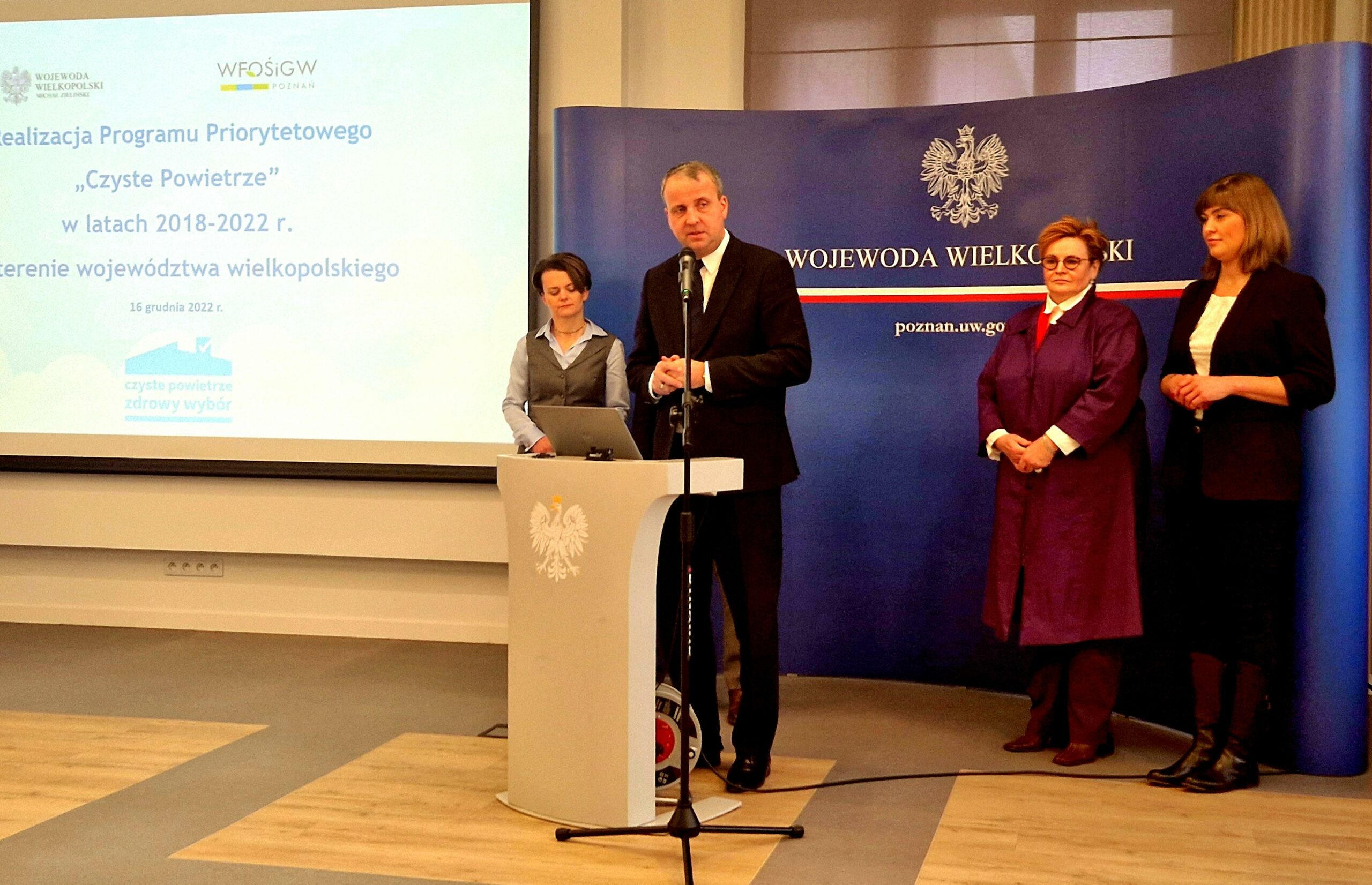 Na zdjęciu jedna osoba stoi przy mównicy, a pozostałe 4 osoby stoją w tle.