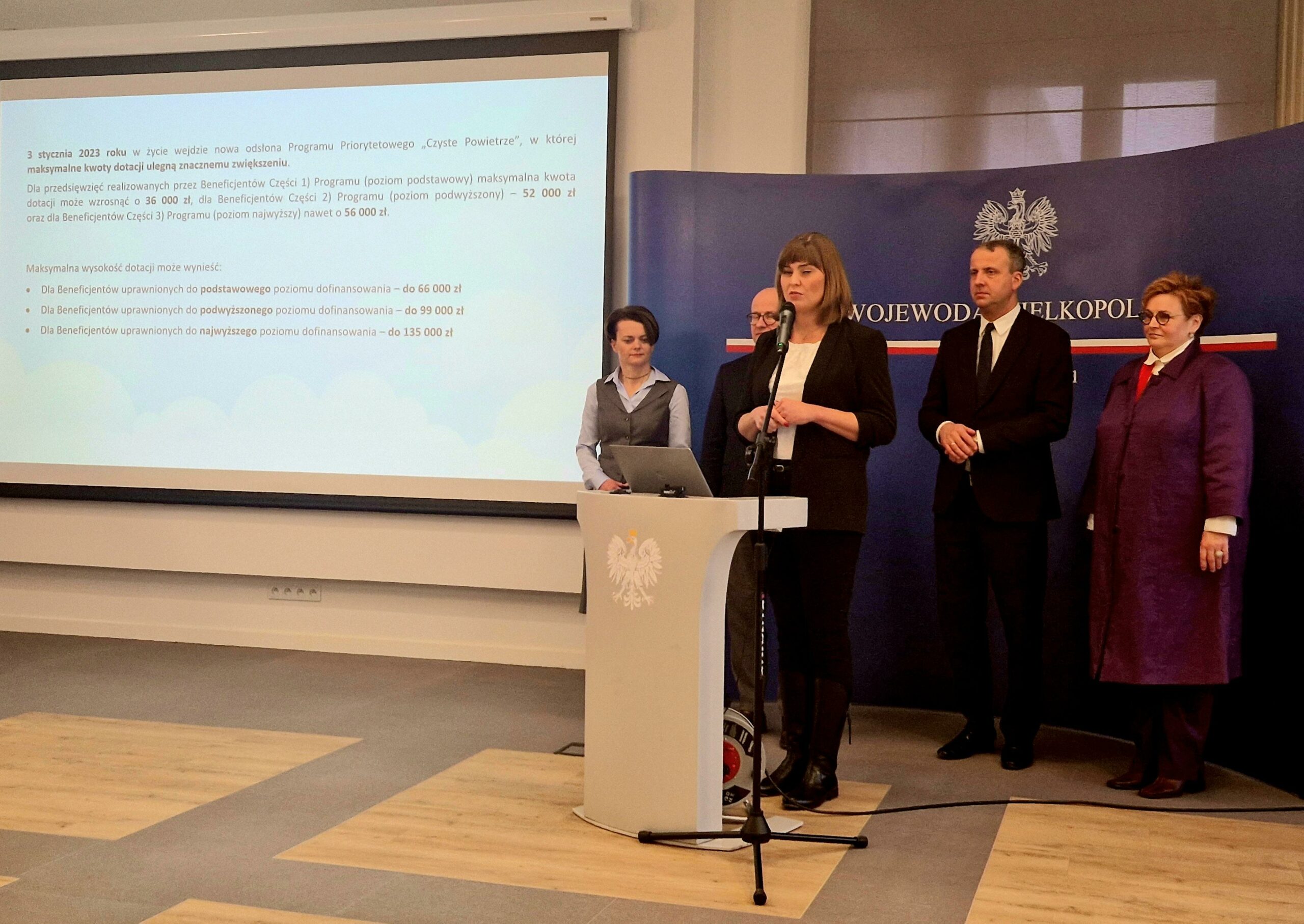 Na zdjęciu jedna osoba stoi przy mównicy, a pozostałe 4 osoby stoją w tle.