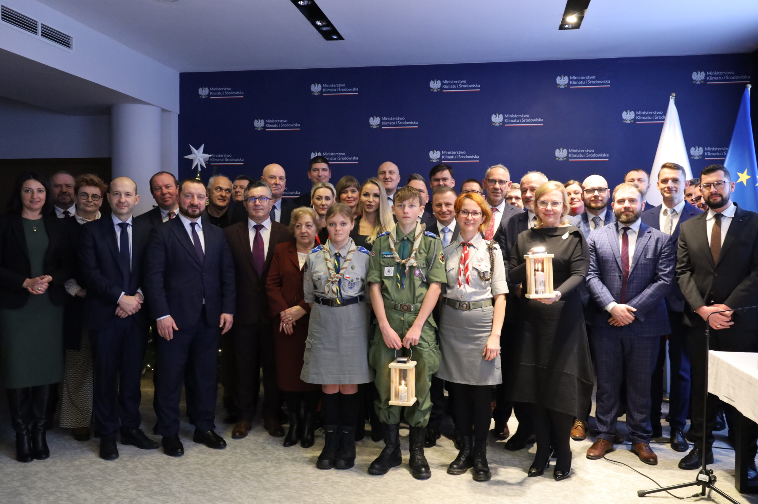 Zdjęcie przedstawia dużą grupę osób na tle niebieskiej sciany.