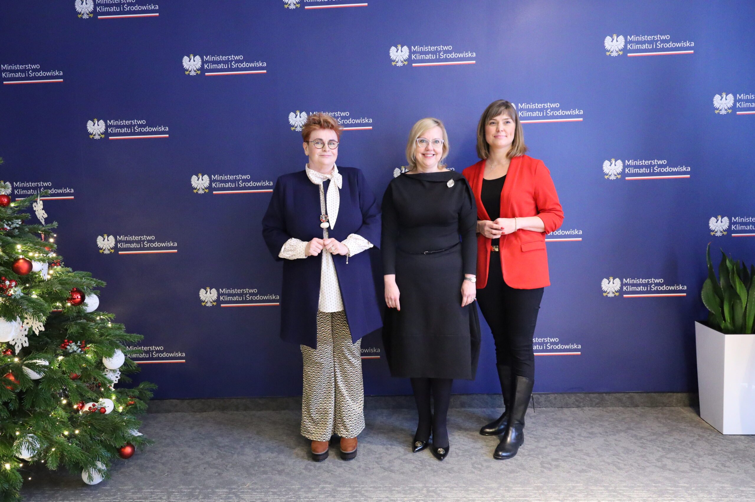 Na zdjęciu znajdują się 3 osoby stojące na tle niebieskiej ściany.