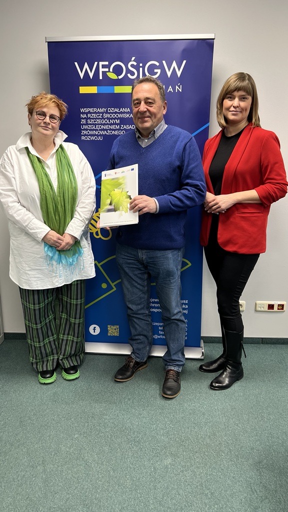 Na zdjęciu stoją 3 osoby na tle ściany.