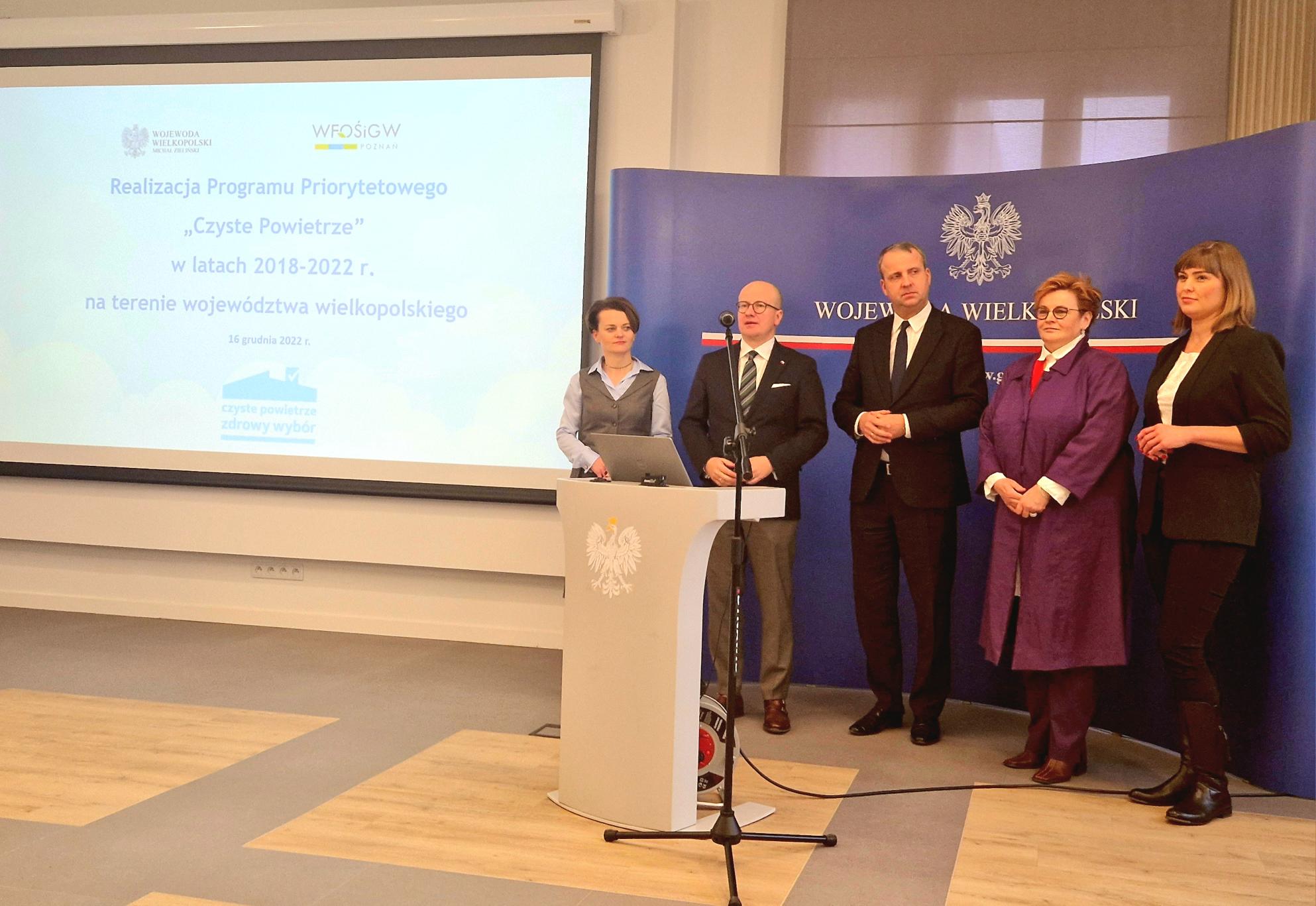 Na zdjęciu znajduje się 5 osób, które stoją na tle niebieskiej ścianki reklamowej.