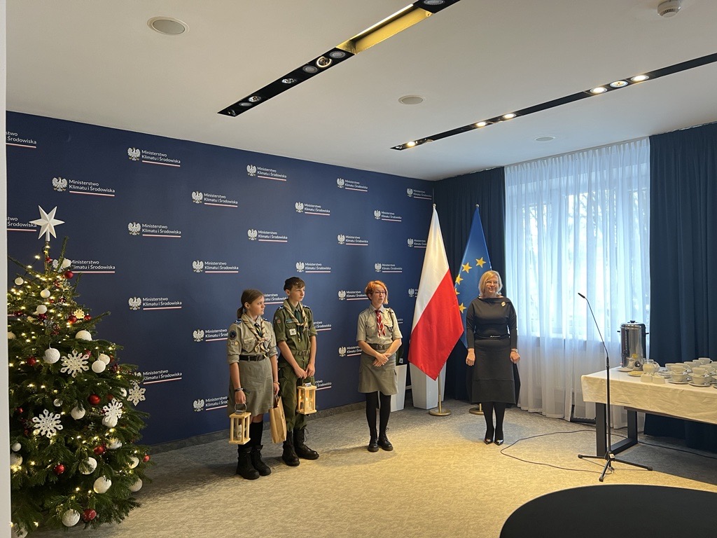 Zdjęcie przedstawia stojące 4 osoby na tle niebieskiej ściany.