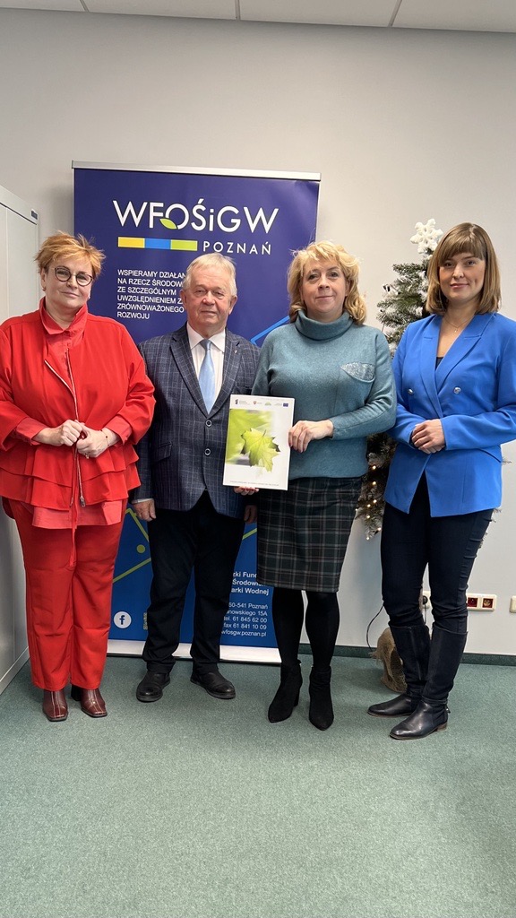 Na zdjęciu stoją 4 osoby na tle ściany i bannera reklamowego.