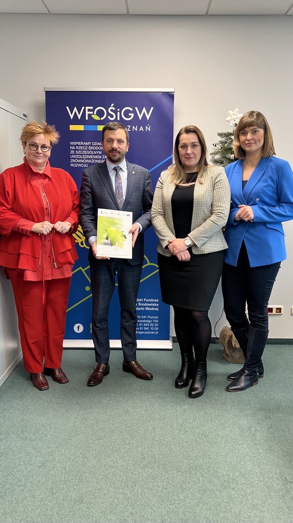 Na zdjęciu stoją 4 osoby na tle ściany i bannera reklamowego.