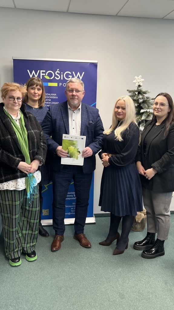 Na zdjęciu znajduje się 5 osób stojących na tle bannera reklamowego.