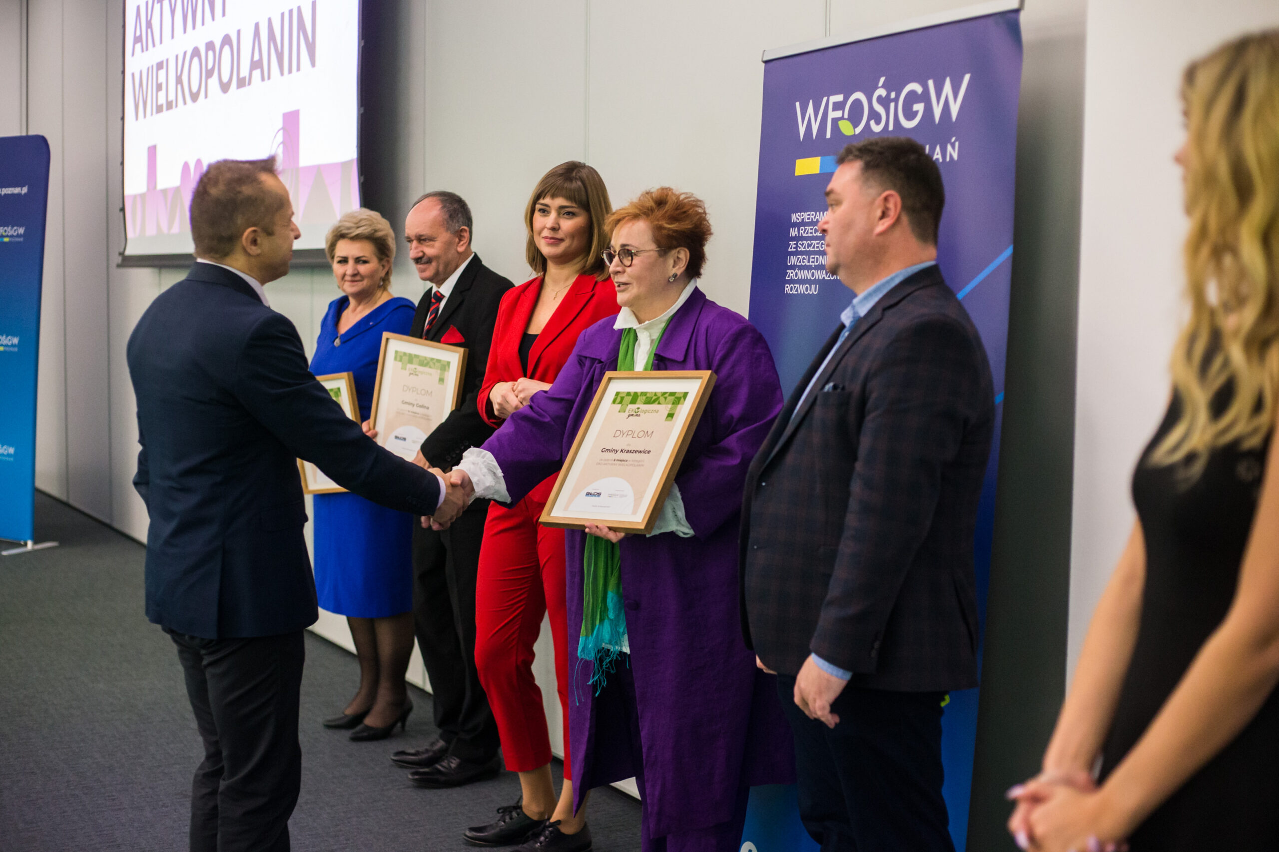 7 osób stoi na tle ściany.