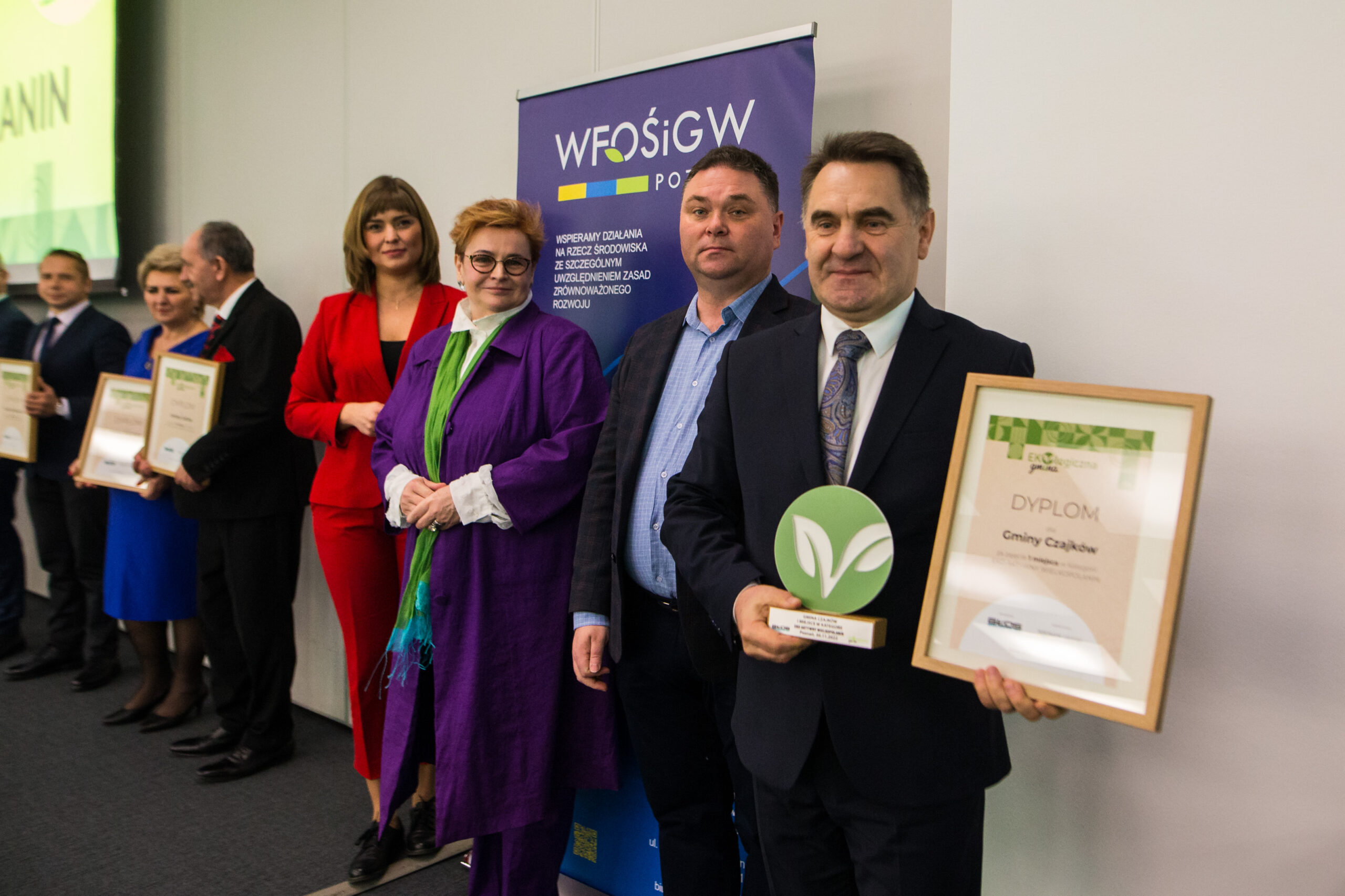 7 osób stoi na tle ściany.