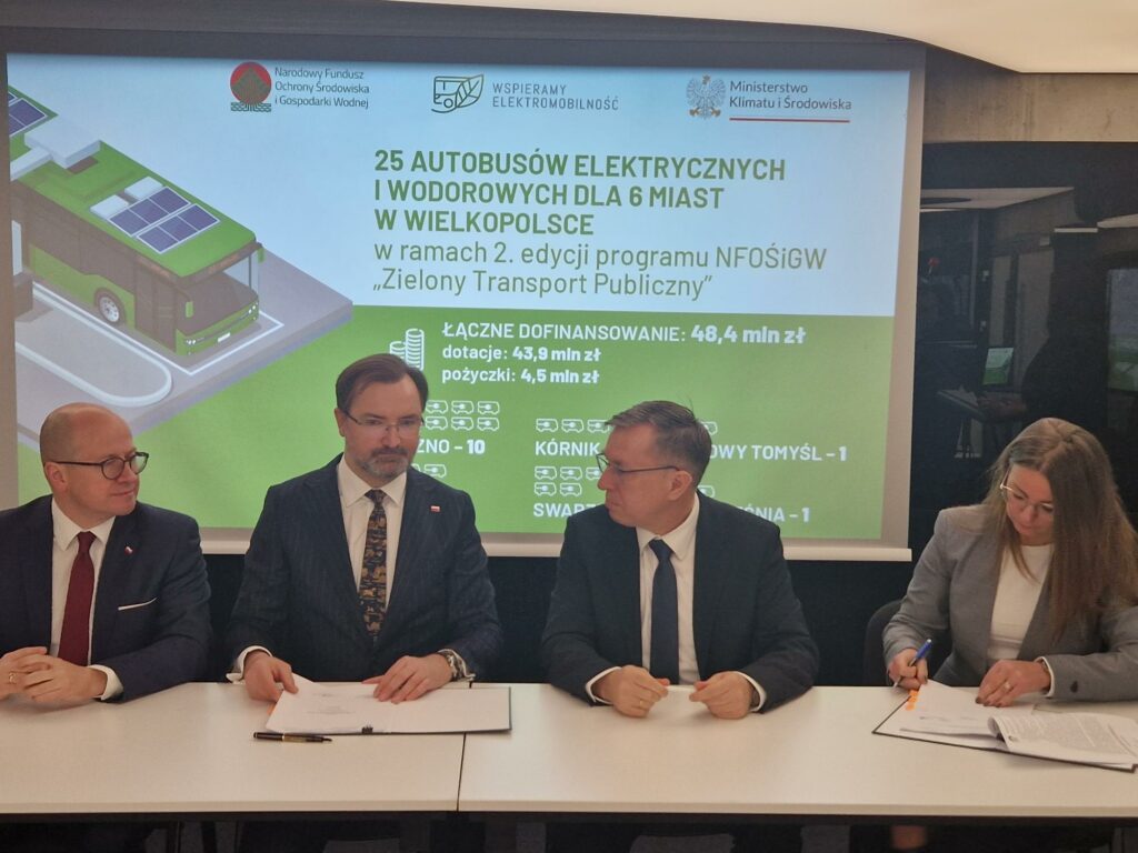 Na zdjęciu 4 osoby siedzą za stołem na tle ekranu.