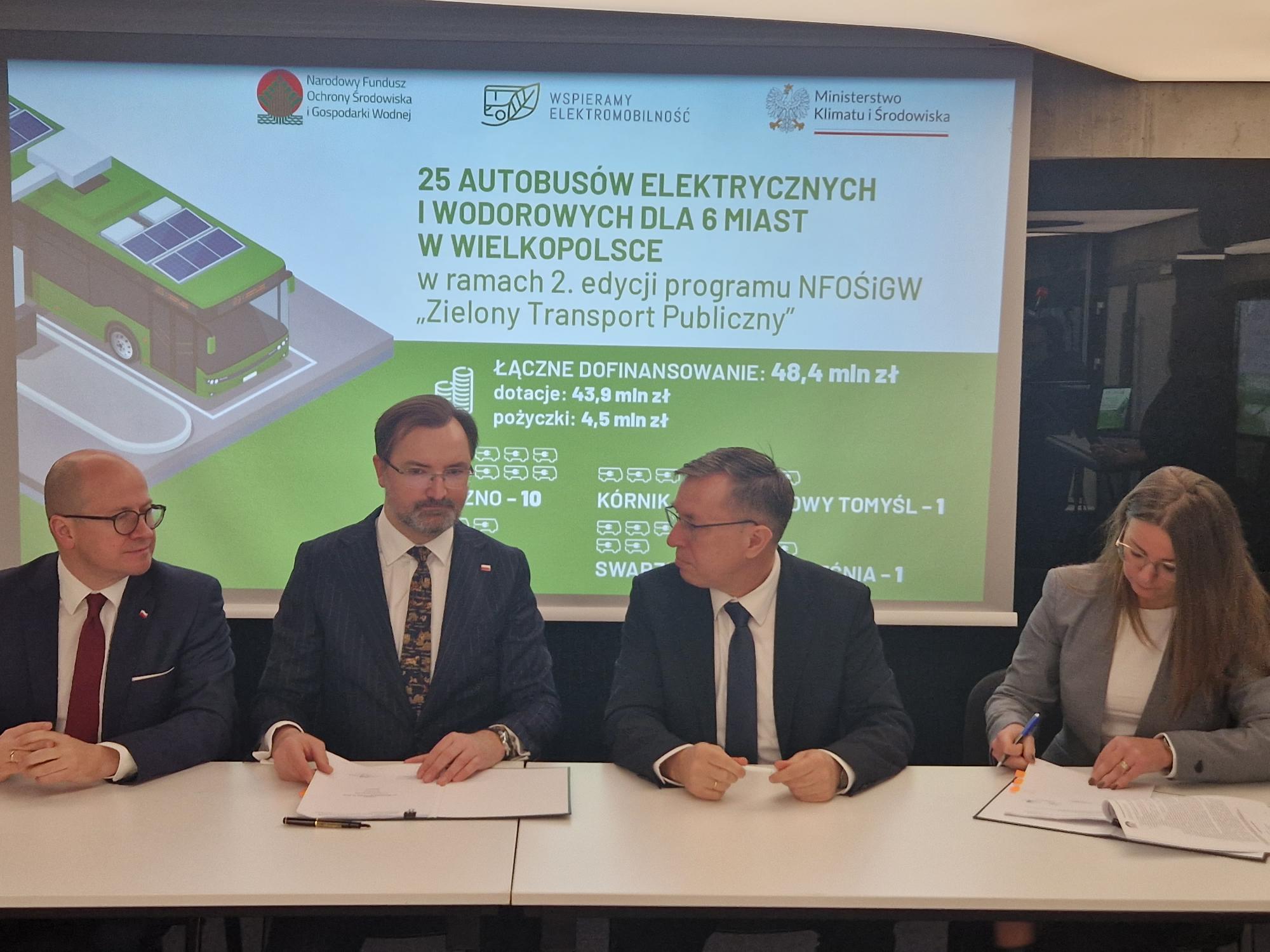 Na zdjęciu 4 osoby siedzą za stołem na tle ekranu.