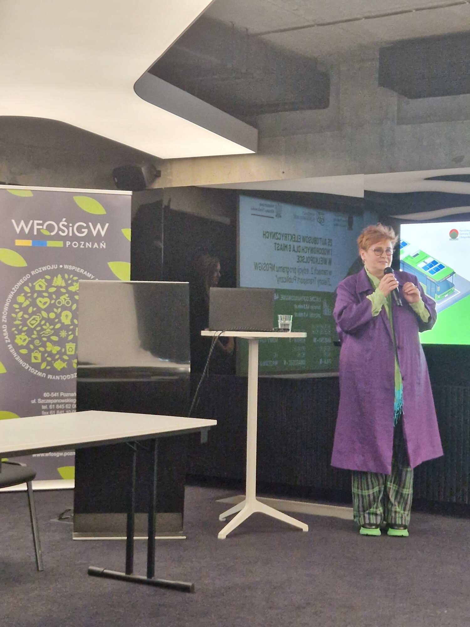 Na zdjęciu stoi jedna osoba z mikrofonem.