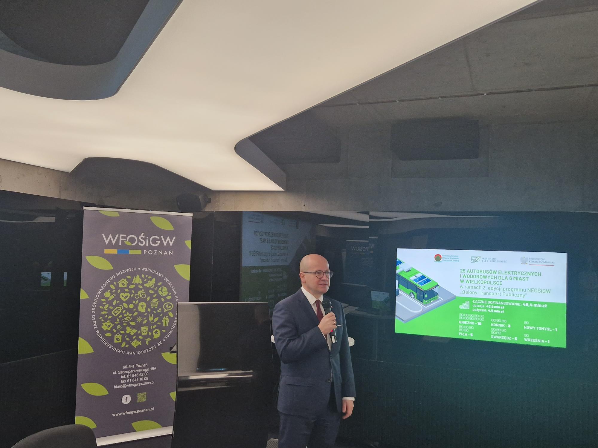 Na zdjęciu stoi jedna osoba, która w ręku trzyma mikrofon.