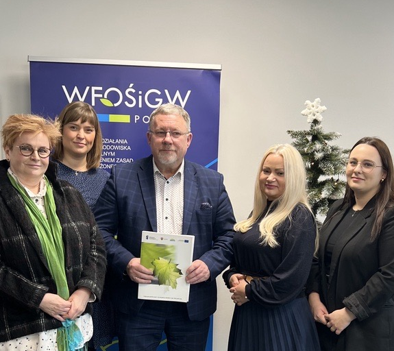 Na zdjęciu znajduje się 5 osób stojących na tle bannera reklamowego.