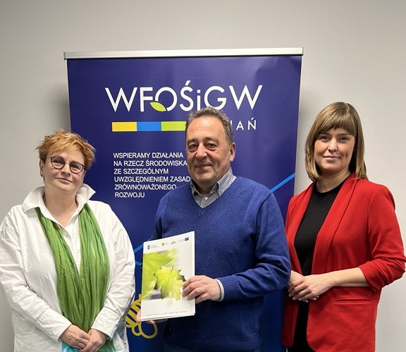 Na zdjęciu stoją 3 osoby na tle ściany.