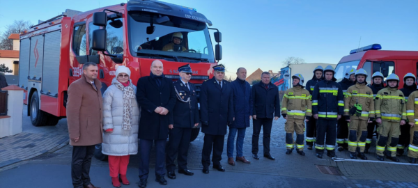Szereg osób stoi przed samochodem strażackim