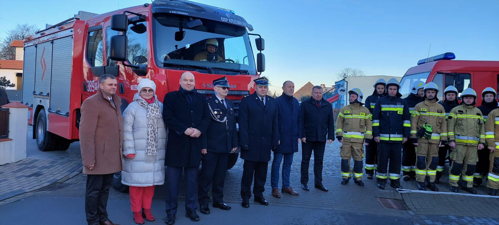 Szereg osób stoi przed samochodem strażackim