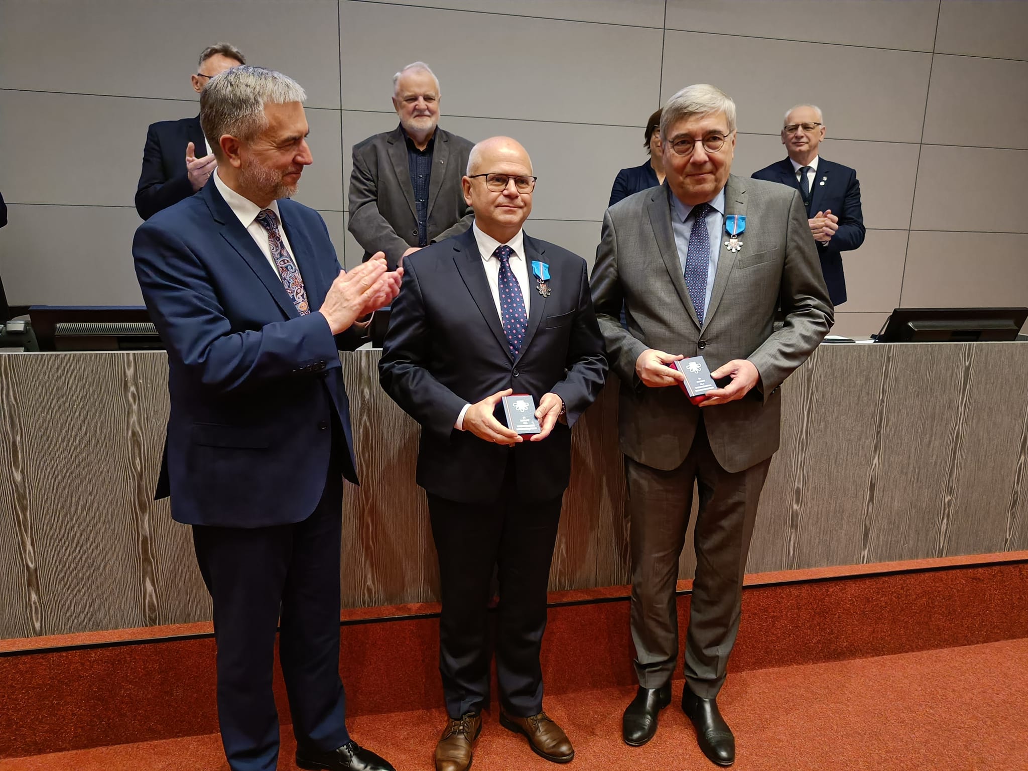 3 osoby stoja na tle sceny.