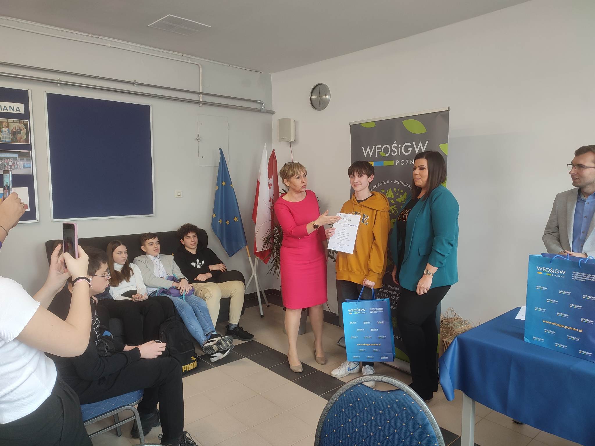 5 osób stoi na tle ściany, jedna wręcza dyplom.