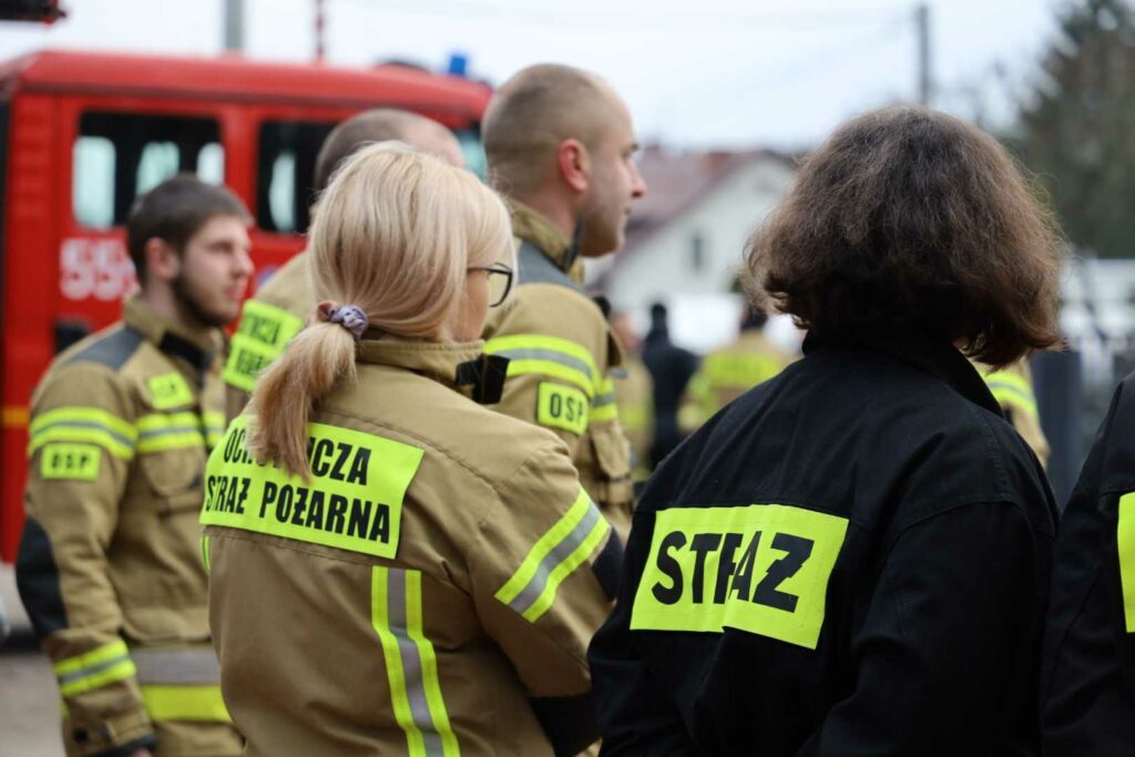 Grupa strażaków przy wozie gaśniczym.