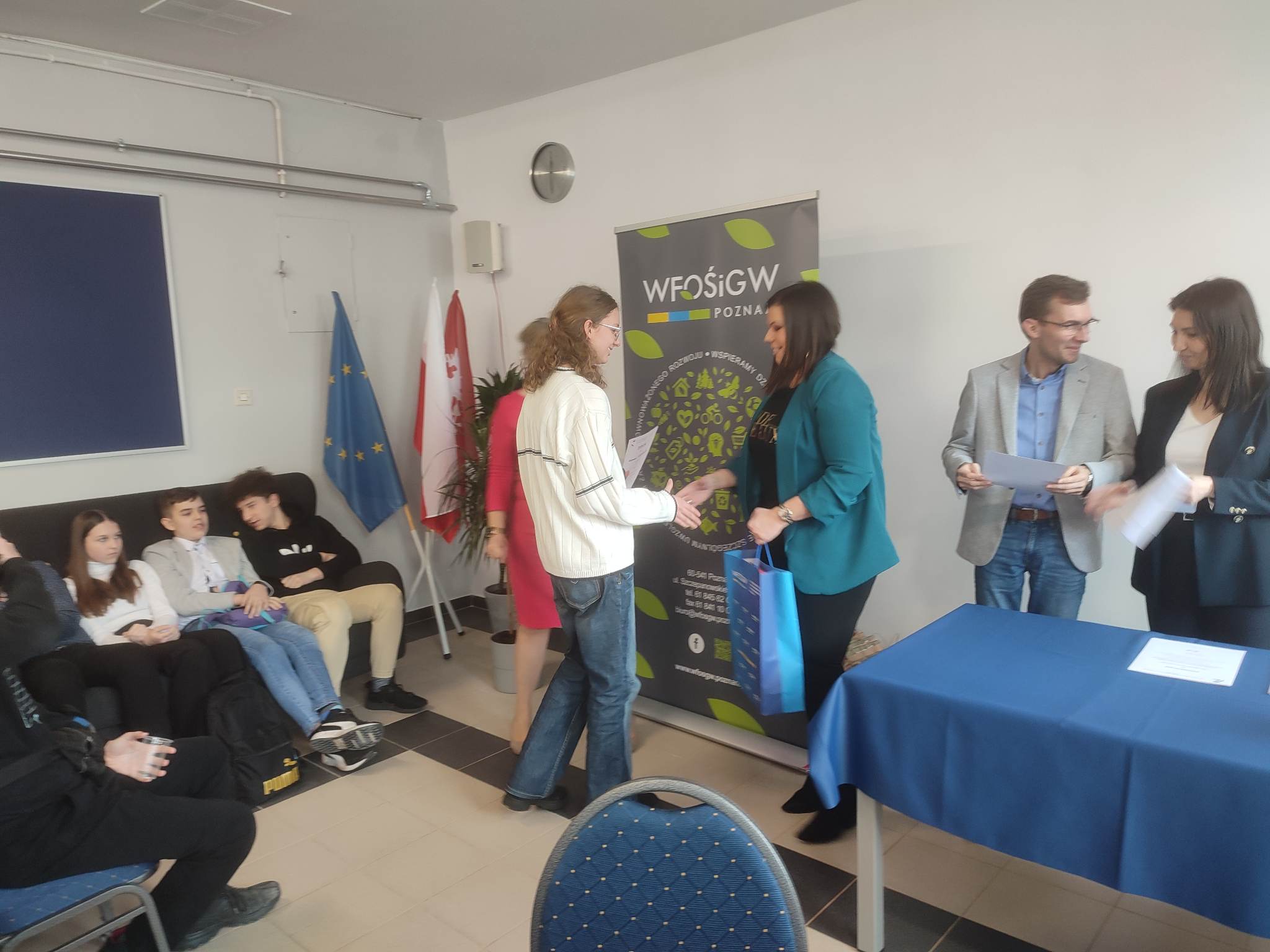 5 osób stoi na tle ściany, jedna wręcza dyplom.