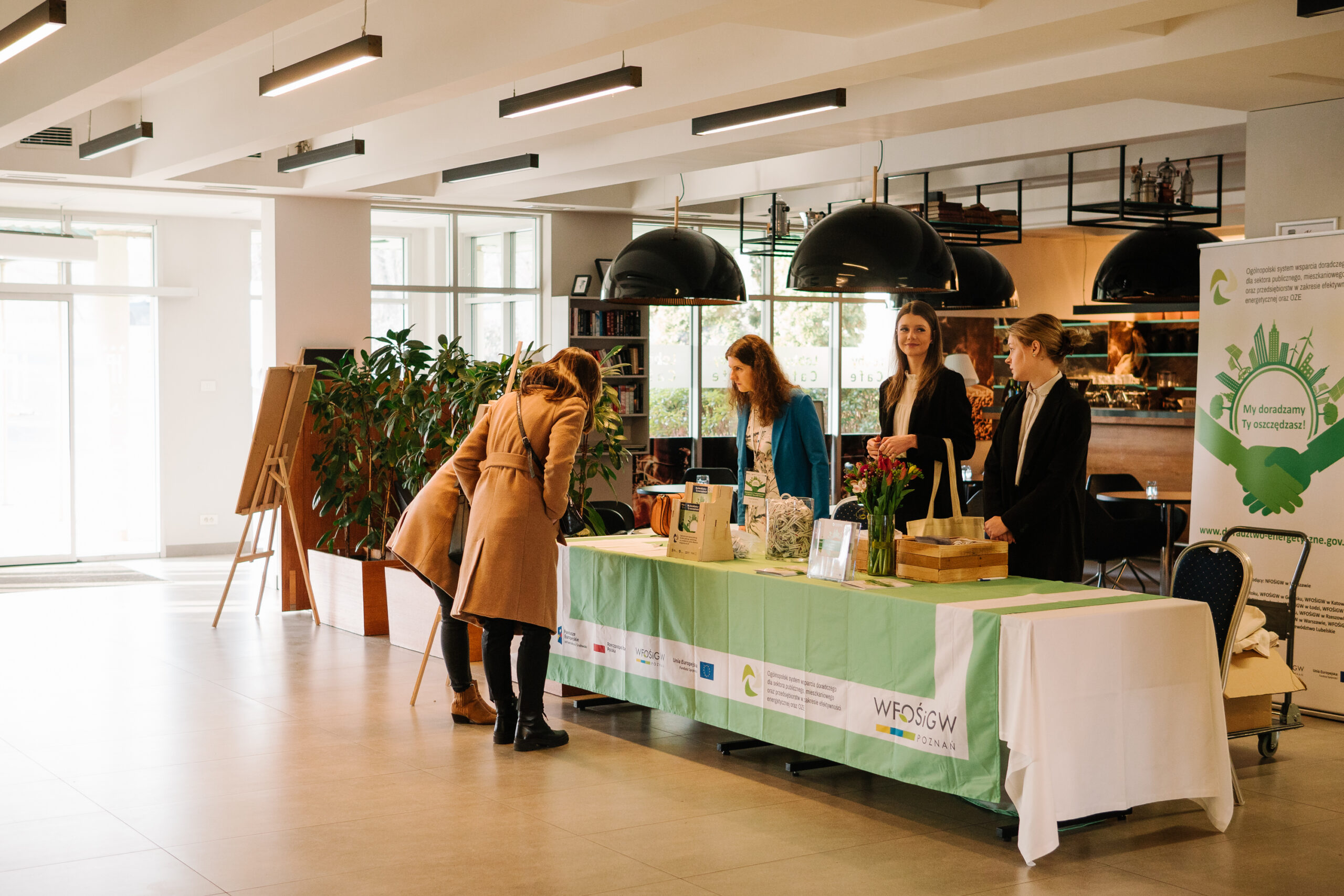 Recepcja konferencji, a przy niej osoba rejestrująca się na konferencję.