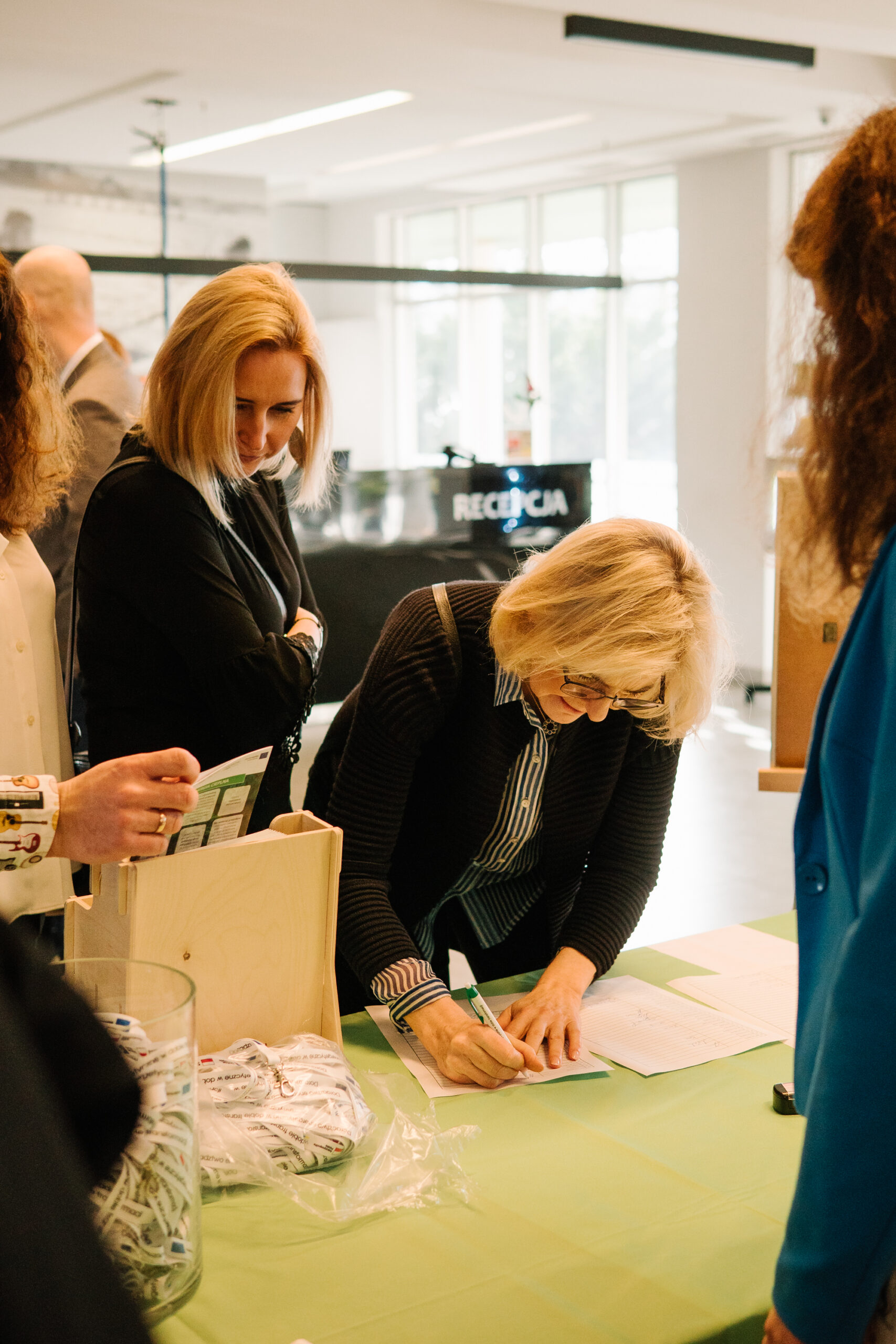 Recepcja konferencji, a przy niej osoba rejestrująca się na konferencję.