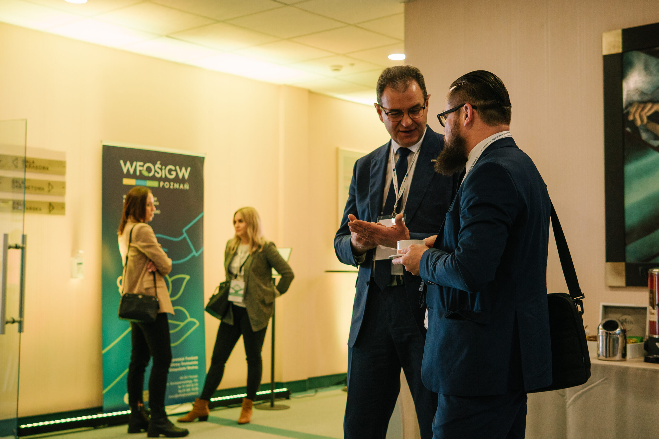 4 osoby na korytarzu przed salą, na której odbywa się konferencja.