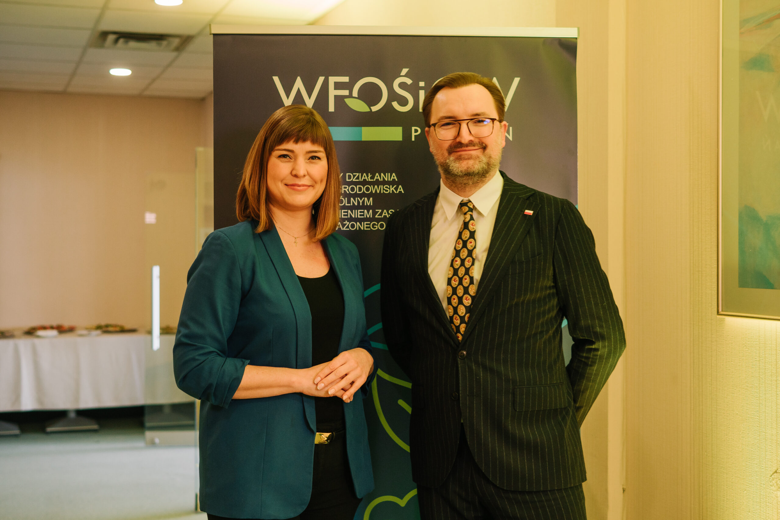 2 osoby stoją na tle bannera reklamowego.