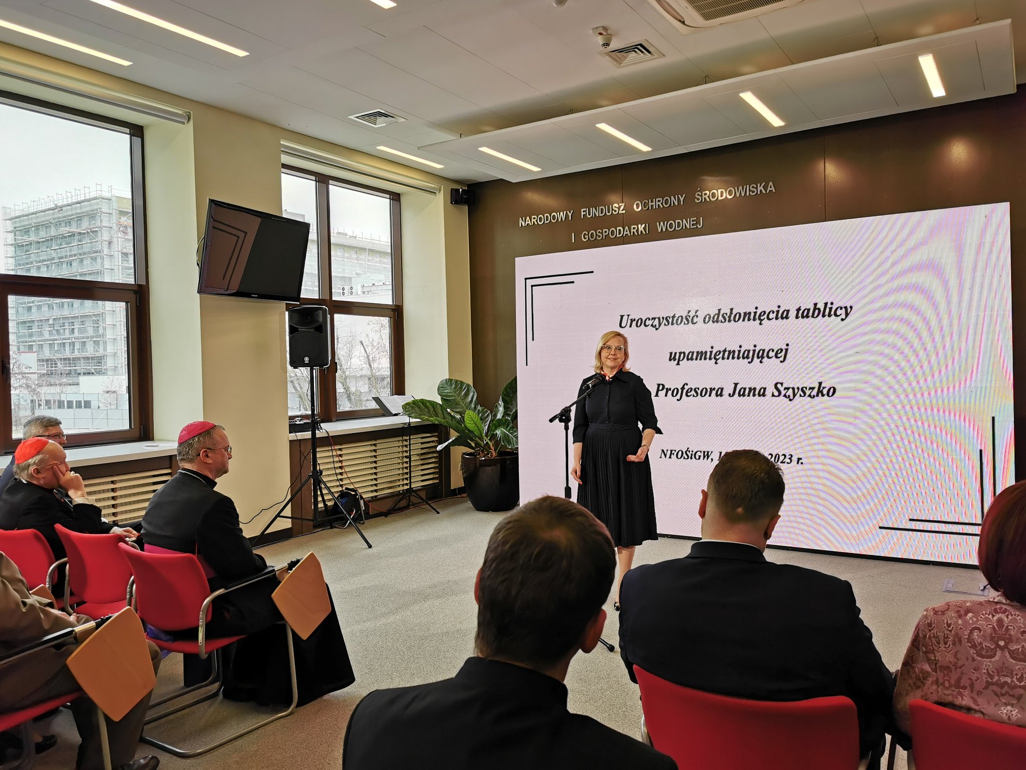 Jedna osoba stoi na tle ściany i przemawia.