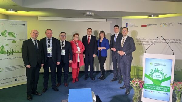 8 osób stoi na tle ściany i bannerów reklamowych.