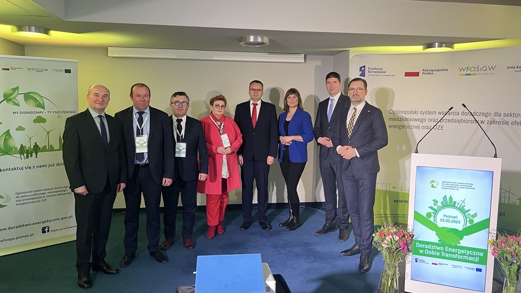 8 osób stoi na tle ściany i bannerów reklamowych.