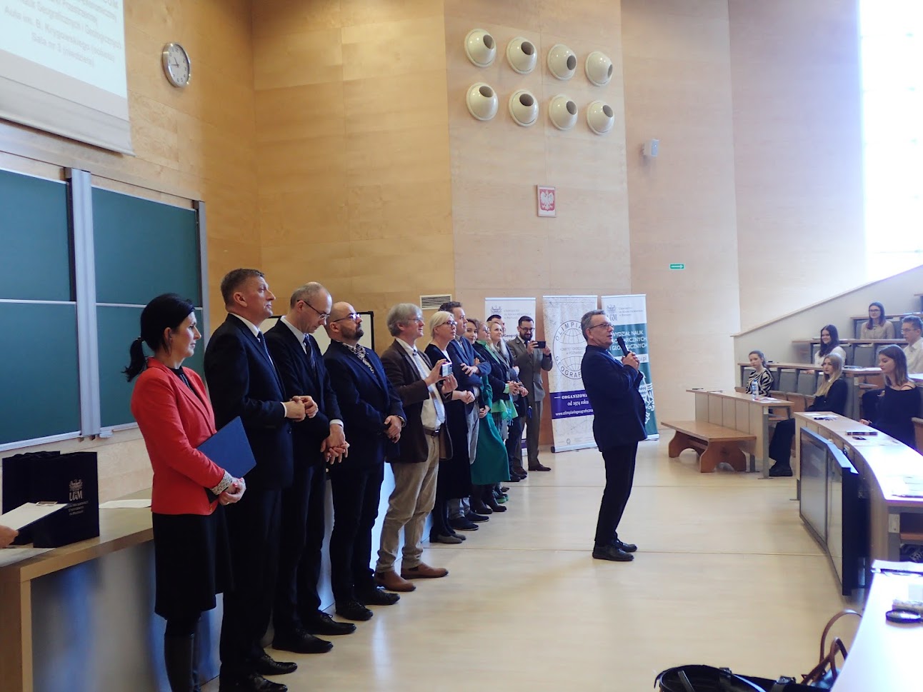 Grupa osób stojąca przed tablicą na sali wykładowej.