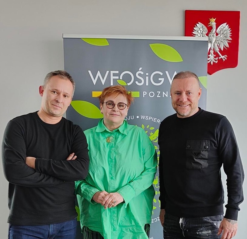 3 osoby stoją na tle ściany w pomieszczeniu.