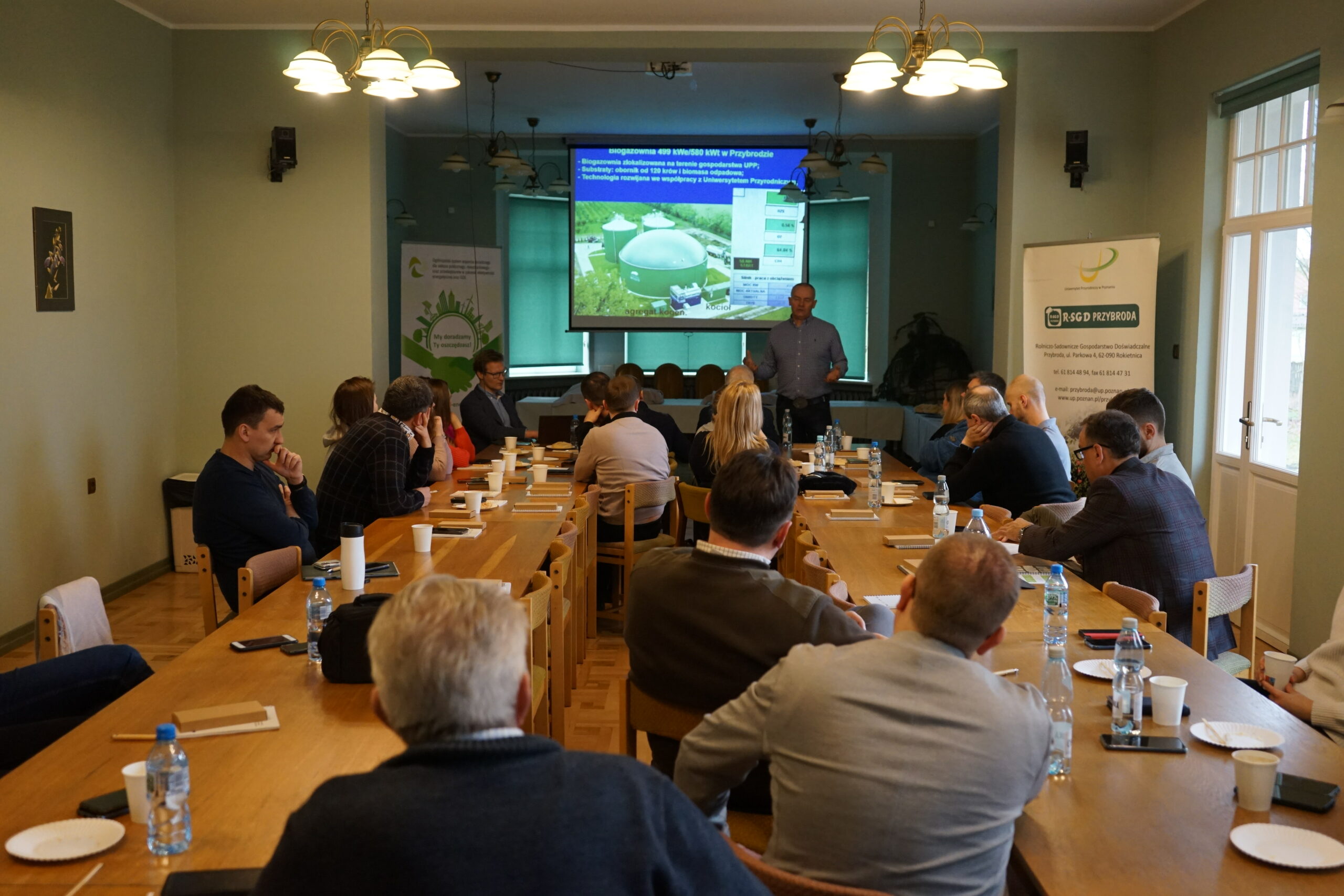 Duża grupa ludzi siedzi na sali i słucha prelekcji patrząc na prezentację.