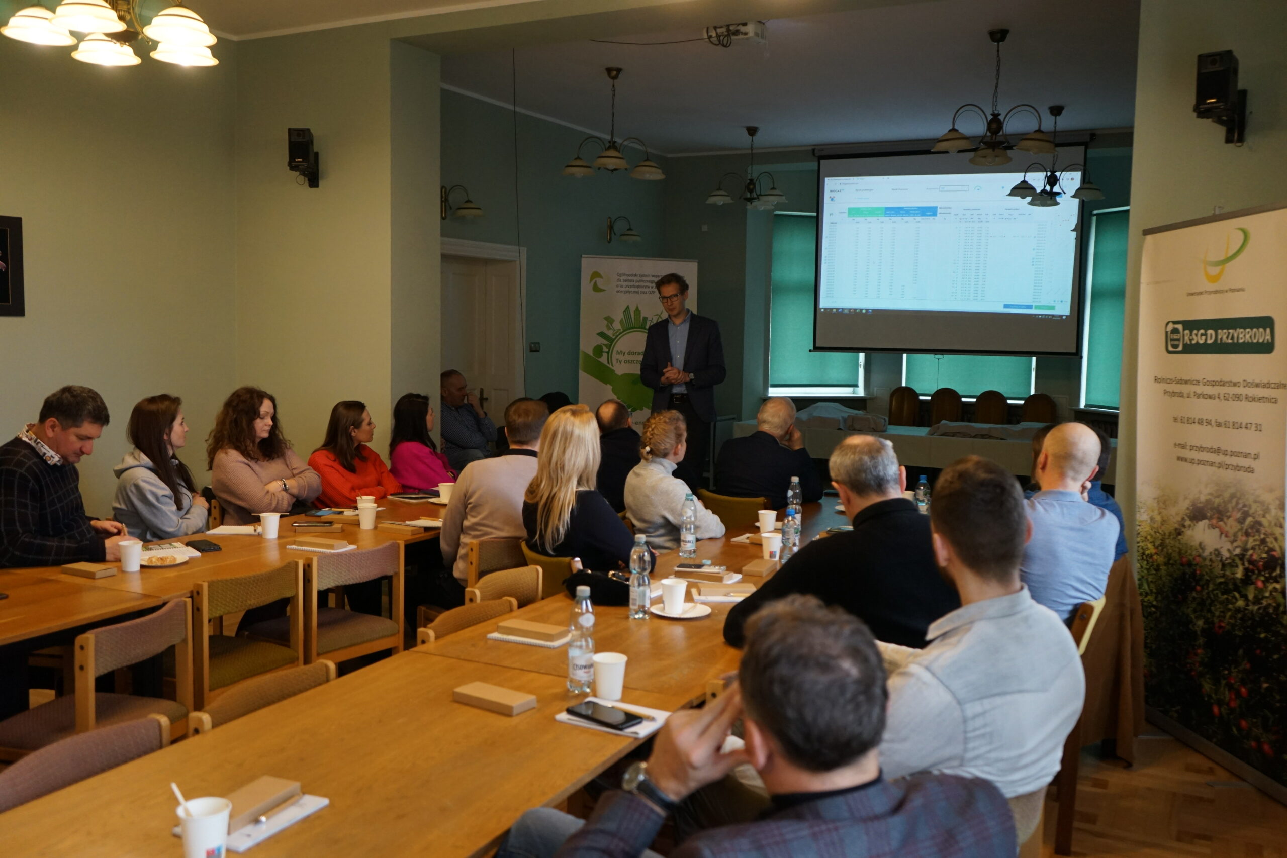 Duża grupa ludzi siedzi na sali i słucha prelekcji patrząc na prezentację.