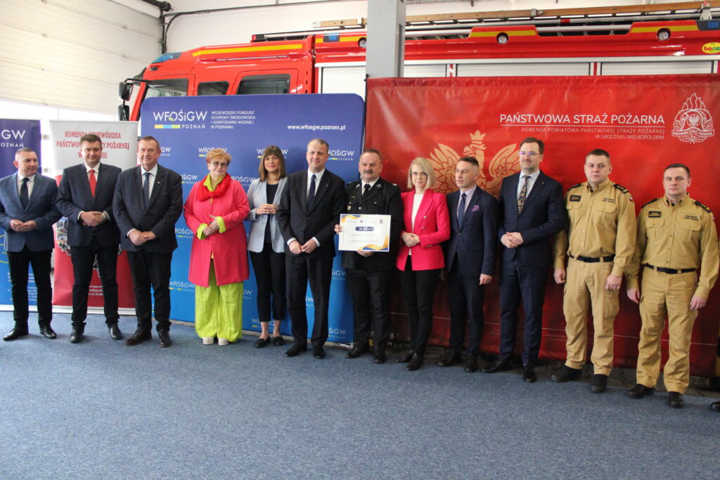 Szereg osób stoi na tle ścianek reklamowych.