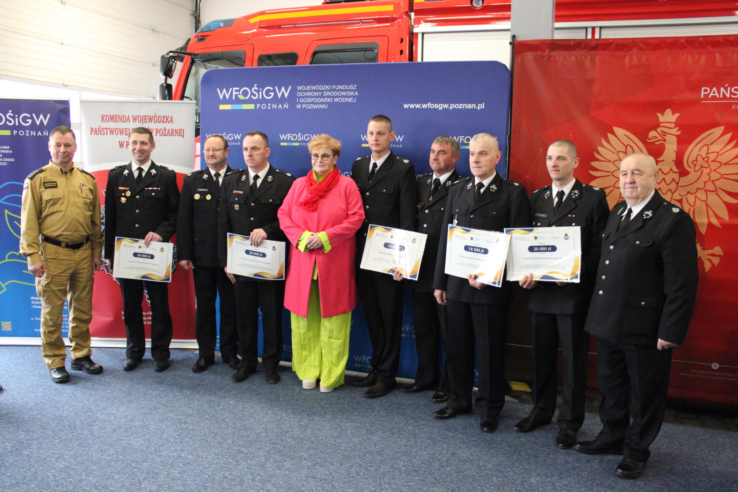 Szereg osób stoi na tle ścianek reklamowych.