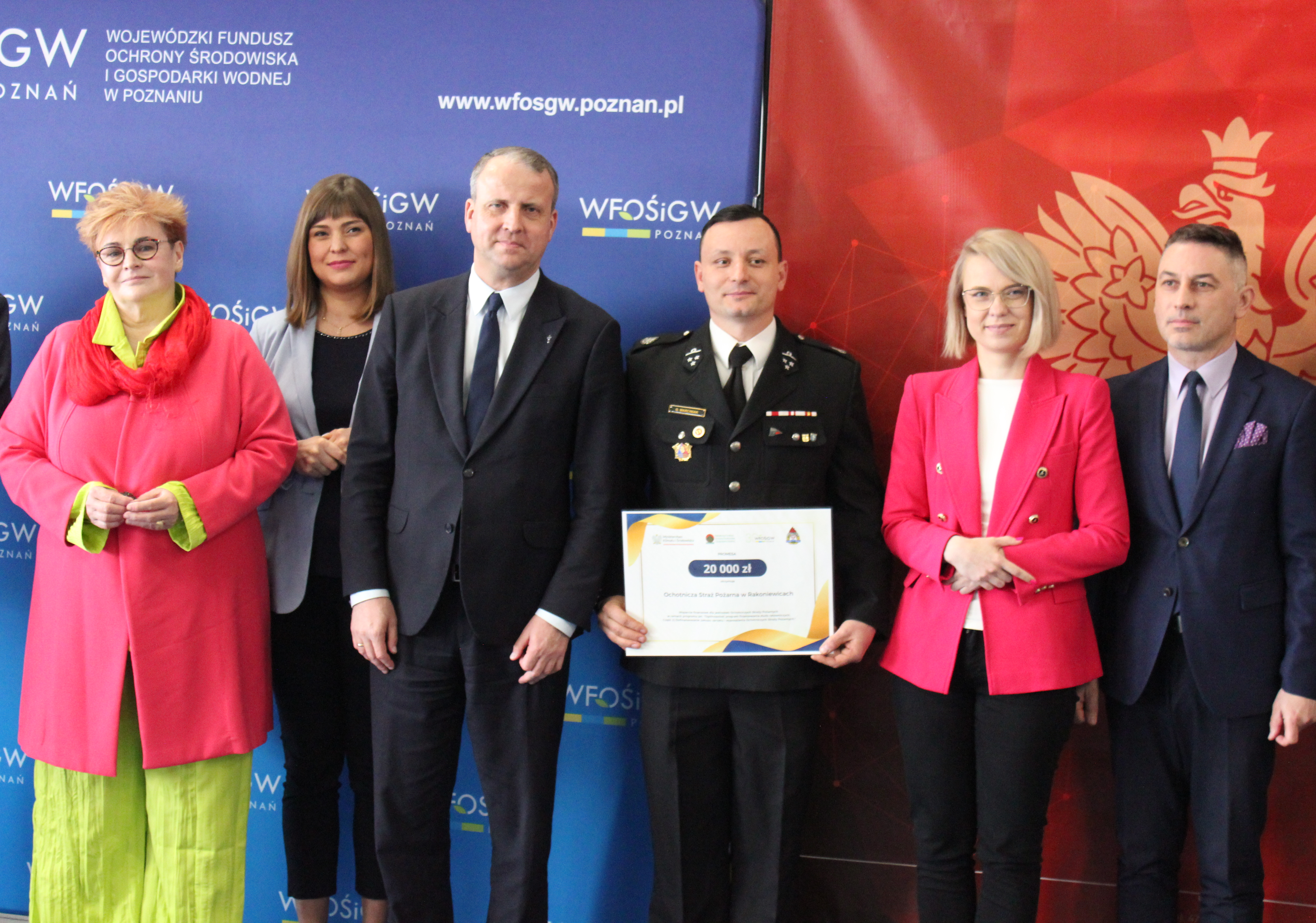 Szereg osób stoi na tle ścianek reklamowych.