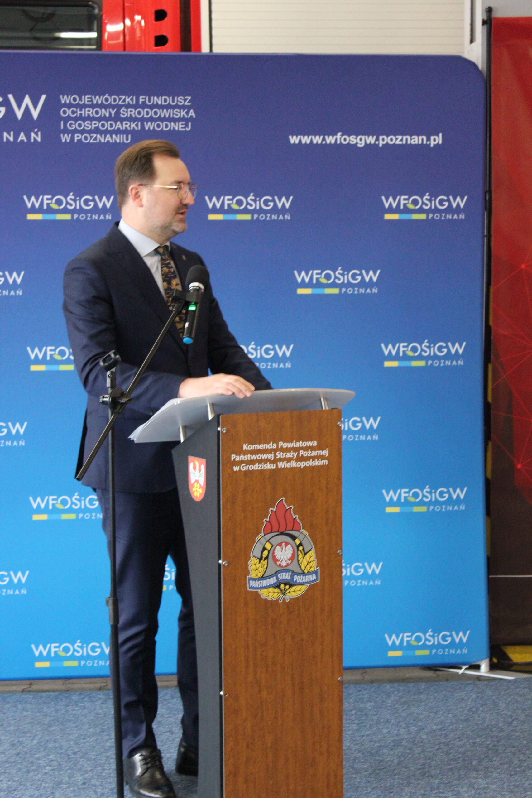 1 osoba stoi przy mównicy i przemawia.