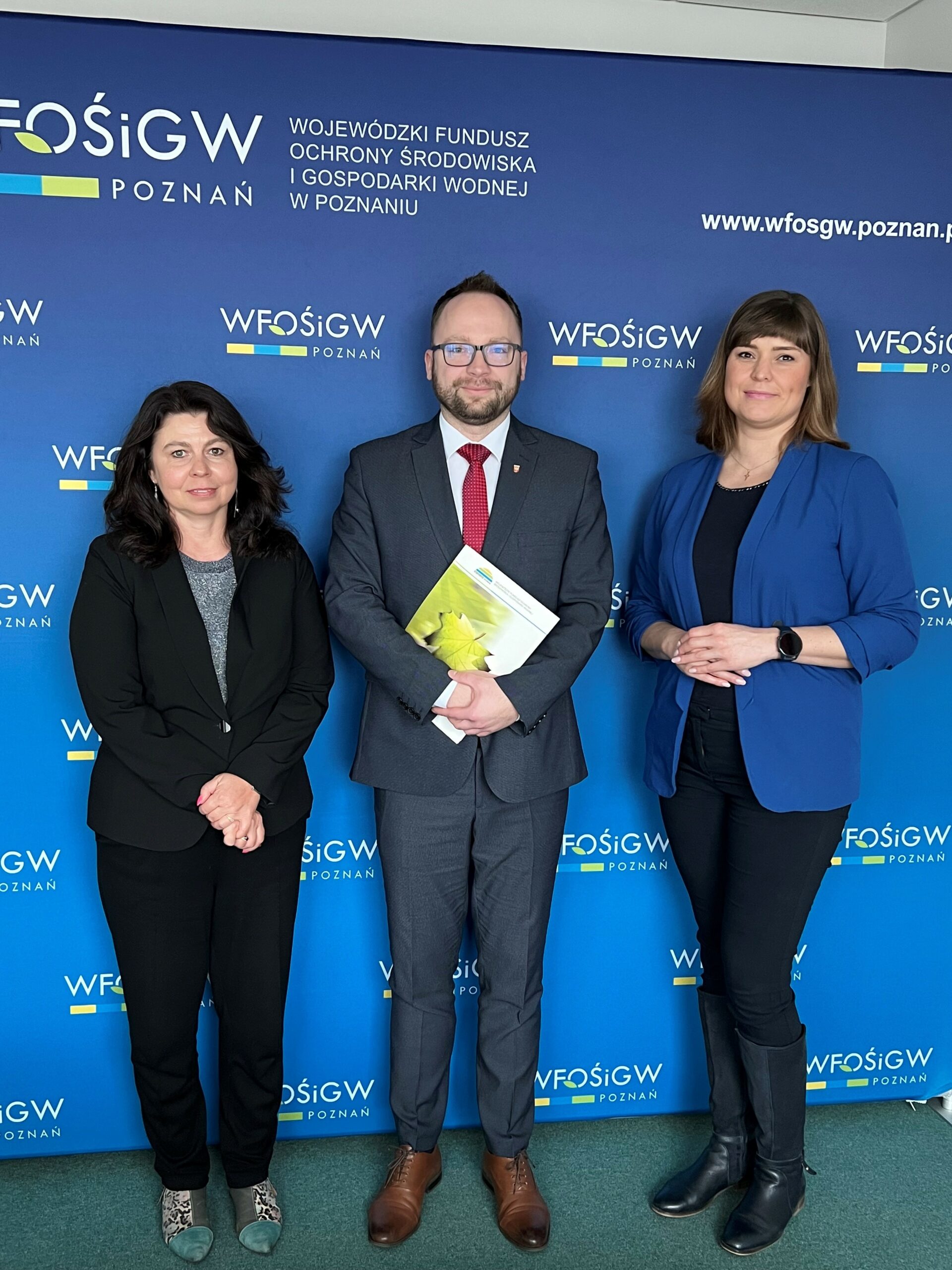 3 osoby stoją na tle ściany.