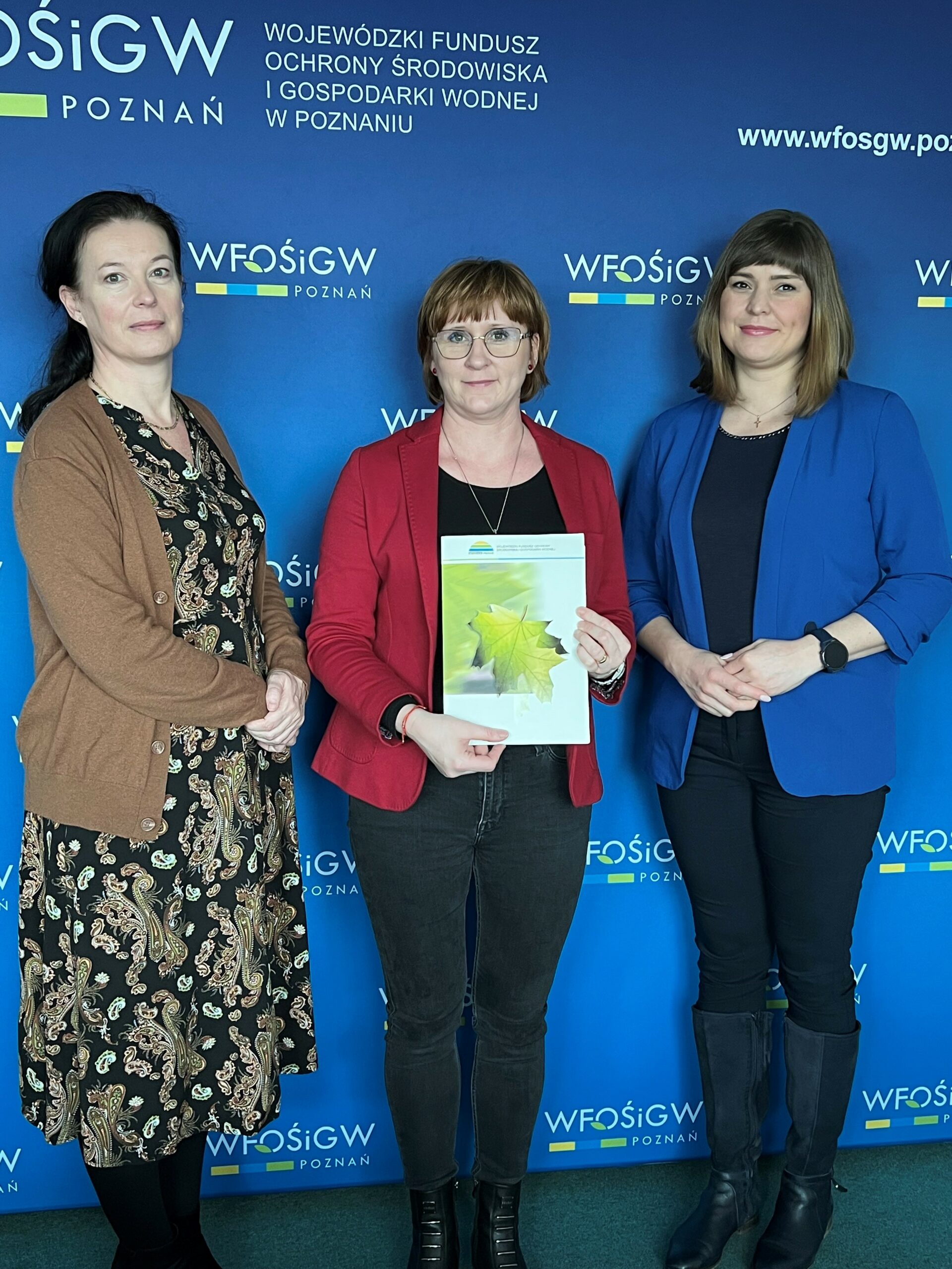 3 osoby stoją na tle ściany.